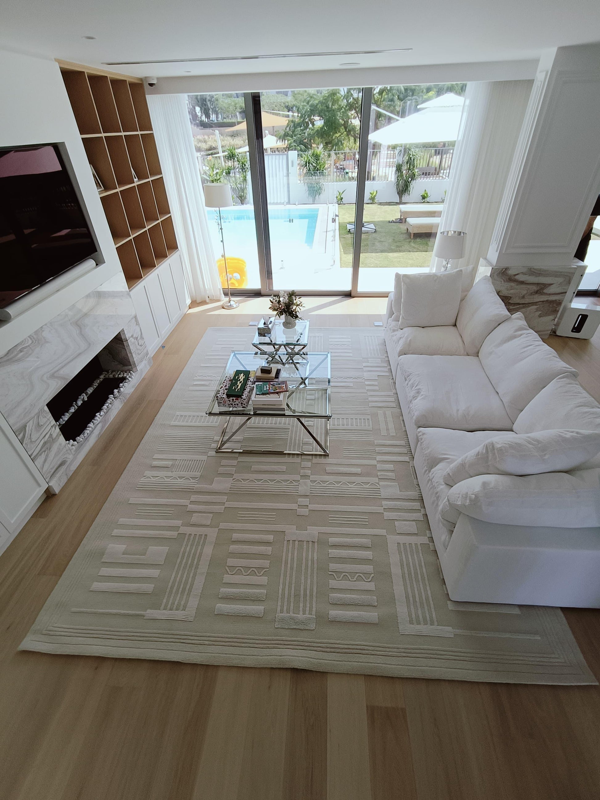 Modern living room with white sofa, coffee table, and rug, featuring a pool view.