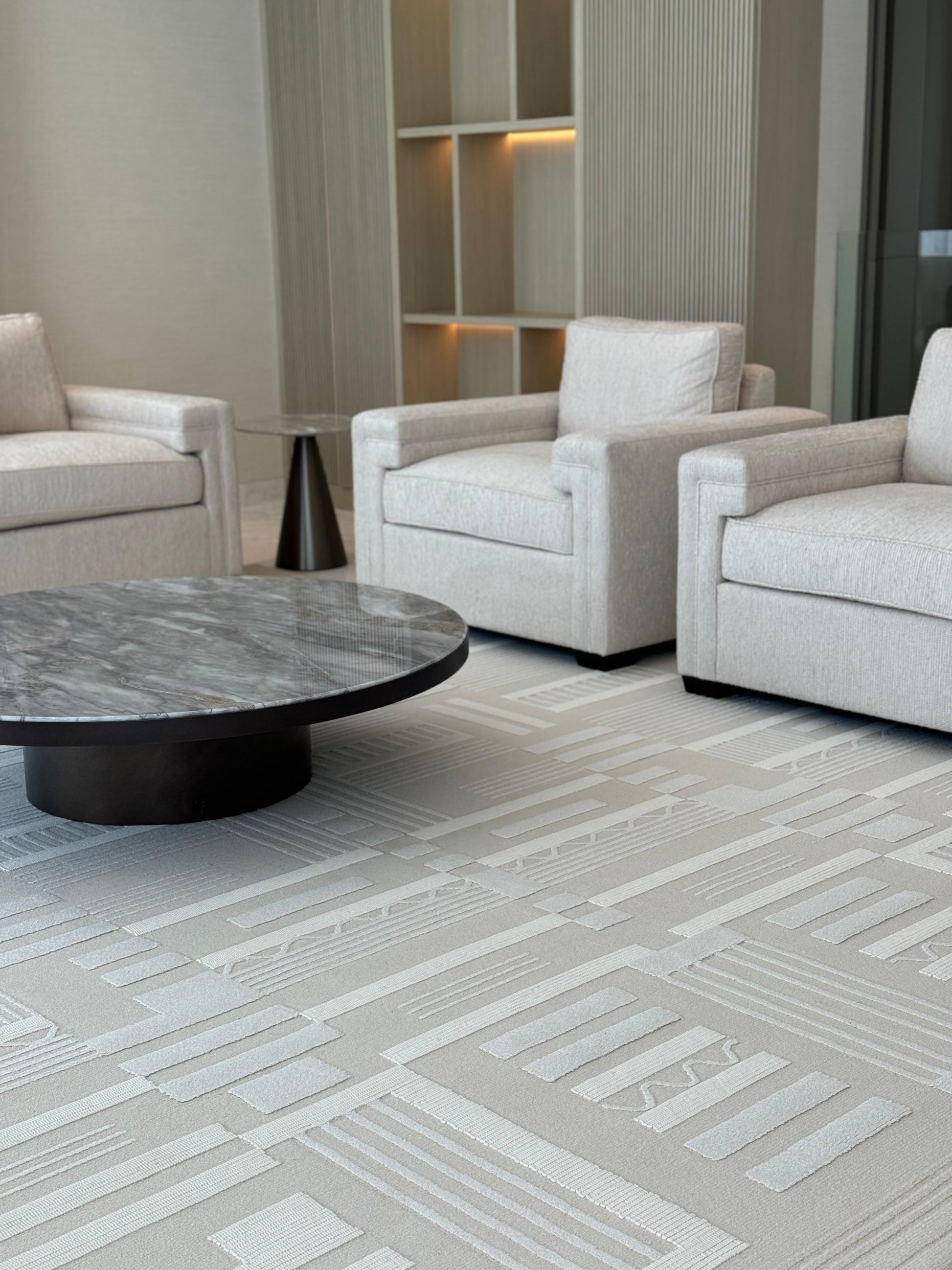 Modern living room with gray upholstered chairs and a round coffee table on a patterned carpet.