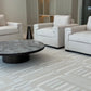 Modern living room with gray upholstered chairs and a round coffee table on a patterned carpet.