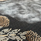 Close-up of a textured rug with geometric patterns in black, gold, and gray.